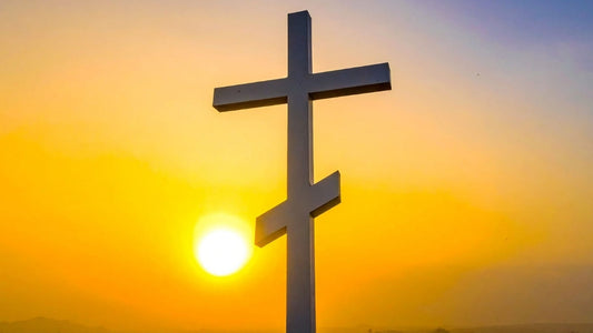 Croix orthodoxe à trois traverses sur fond de soleil couchant, symbolisant la foi chrétienne.