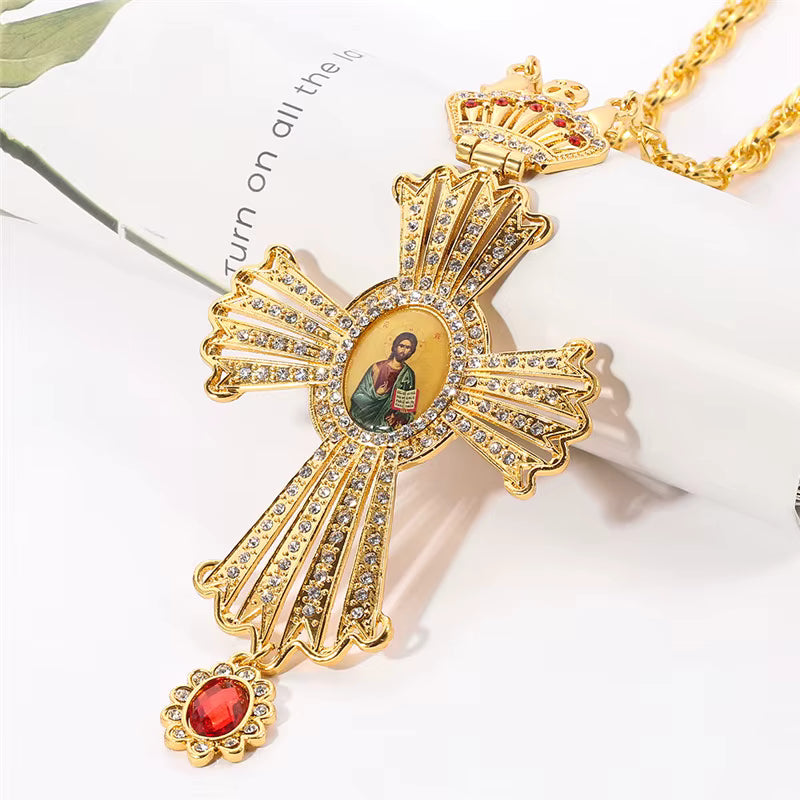 Pendentif croix byzantine dorée avec icône et chaîne, orné de cristaux et d'une pierre rouge.