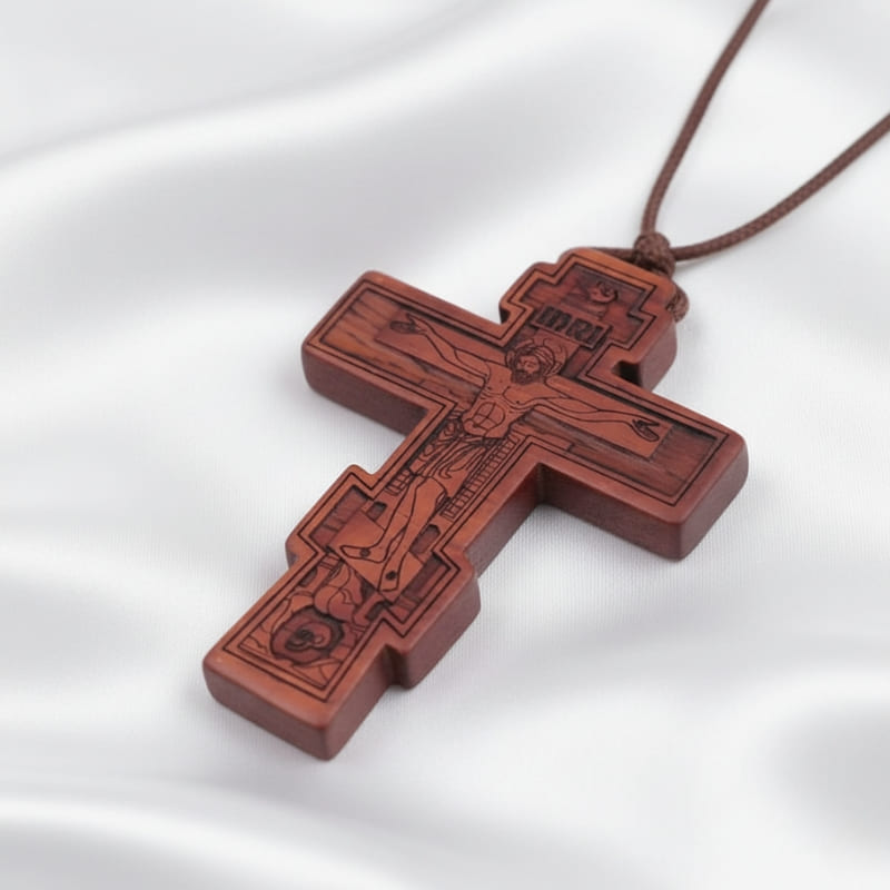 Collier croix orthodoxe en bois marron clair posé sur de la soie blanche