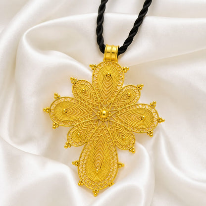 Pendentif croix éthiopienne en fleurs posée sur un tissu en soie blanc 